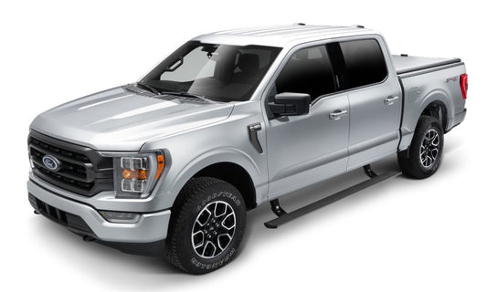 A Ford F150 is parked on a white background, featuring black trim, side steps, and sleek black alloy wheels. This modern, rugged vehicle boasts a crew cab and a bed with cover. Its tinted windows complement the advanced AMP Research PowerStep Plug N Play electric-powered running boards for seamless access.