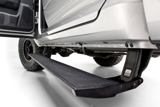 Close-up of a vehicle's AMP Research 22-23 Chevy/GMC Silverado/Sierra 1500 & 2024 2500/3500HD Double/CC PowerStep Xtreme, engineered to aid entry and exit even in sub-zero temperatures. The black step is mounted beneath the silver body with the vehicle door open and the wheel visible in the background, making it perfect for demanding environments.