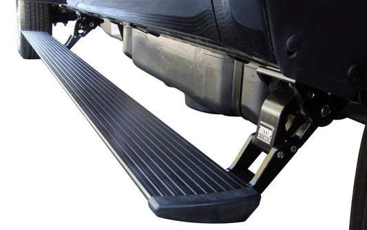 A close-up shows an AMP Research PowerStep, specifically the 2011-2014 GMC Sierra 2500/3500 Extended/Crew model in black, extending from the side of a black vehicle. This electric-powered running board features a textured surface for enhanced grip and is engineered for all-weather performance with an automatic mechanism discreetly installed beneath the vehicle.