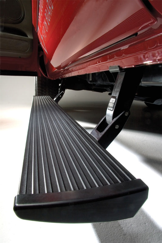 A close-up view of the AMP Research 2015-2018 Ford F150 All Cabs PowerStep Plug N Play - Black, extended below a red truck door. The electric-powered step from AMP Research features a grooved, textured black surface for grip and is supported by a metal arm, ensuring improved ground clearance for any terrain.