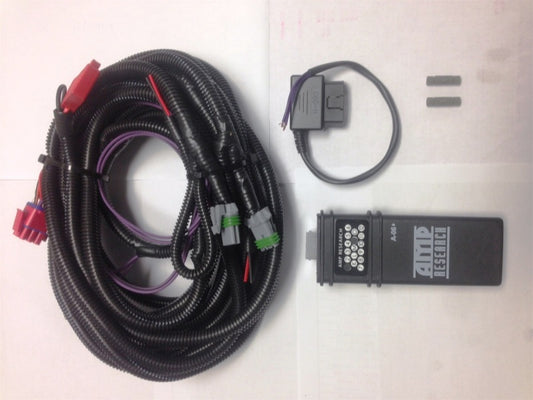 Displayed on a table is the AMP Research 2008-2016 Ford F250/F350 PowerStep Plug N Play - Black, an electronic wiring kit ideal for upgrading your automatic running board. It includes a coiled cable with connectors, a circular loop of wire, and a small black device marked "AMP Research," along with two small metal pieces designed for all-weather performance.