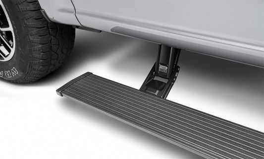 Close-up of an AMP Research PowerStep Plug N Play, a model specifically designed for the 22-23 Ford F-250/350/450 All Cabs with Sync 4, shown as an electric-powered running board extended beneath the side door. The step features a textured surface for grip, while you can also see part of the vehicle’s metallic gray body and tire.