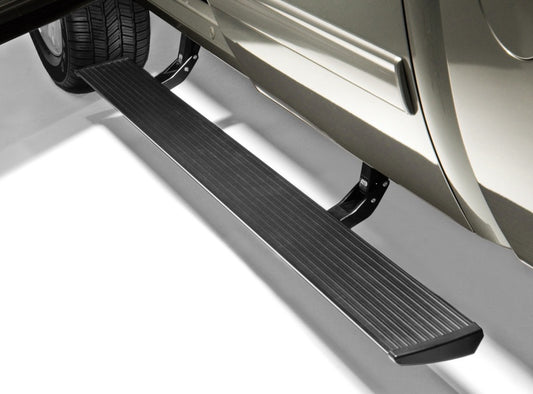 Close-up of a Chevy Silverado 2500/3500 with an AMP Research PowerStep in black extended. This PowerStep offers a ribbed, textured surface and is mounted below the door on a dark bracket, ensuring easy access to the cabin. A visible tire and part of the vehicle's body highlight its sleek design.