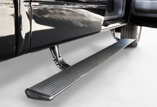 A close-up view of the AMP Research 2004-2008 Ford F150 All Cabs PowerStep, crafted by AMP Research, reveals an electric-powered running board extended from the side of a black vehicle. Made of metal with a textured surface, it is mounted below the open car door, set against a backdrop of light gray pavement.