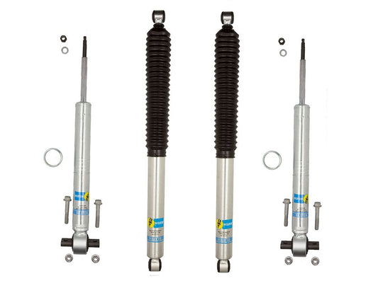 The image showcases the LTW Motorsports 09-13 Ford F-150 2WD Leveling Kit complete with Bilstein 5100 Shocks against a pristine white background. Two shock absorbers feature black rubber boots, while the others do not. Alongside the shocks, various small components like washers and bolts are neatly arranged to offer increased ground clearance with an optional extended length struts setup.