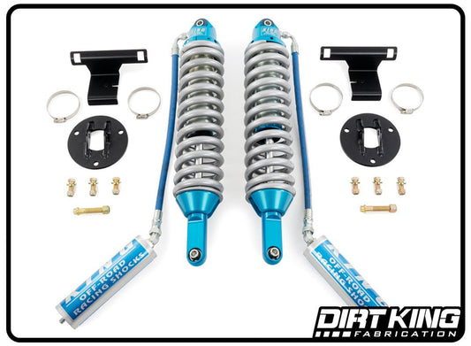The image showcases a Dirt King 19-24 GM 1500 Long Travel Spec King Coilovers kit from DIRT KING SHOCKS designed for off-road performance. It includes two blue and silver coilover shocks with remote reservoirs, mounting brackets, plate mounts, metal clips, bolts, and screws. The DIRT KING SHOCKS logo is at the bottom right.