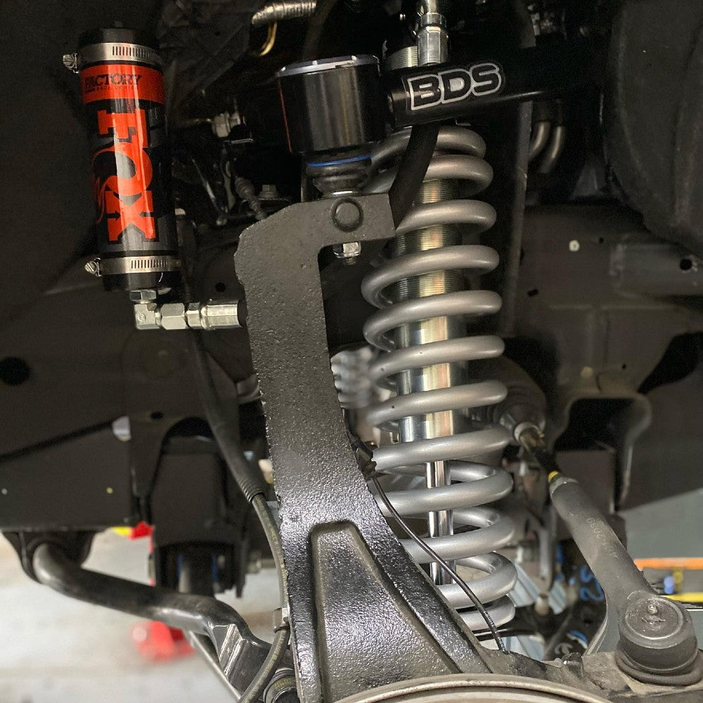 Close-up view of a vehicle's suspension system featuring a large coil spring, shock absorber, and components from brands BDS and FOX. The image highlights the intricate details of the mechanical parts, showcasing their build and assembly.